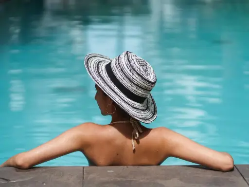 Donna con cappello a righe, braccia aperte, si gode il sole in piscina.