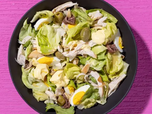Insalata di pollo ricca con lattuga, uova sode, olive verdi e acciughe, condita con maionese.