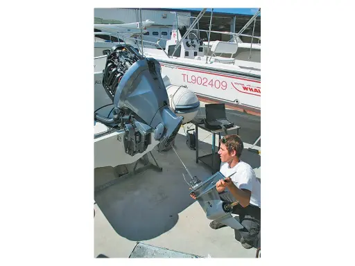 Un mécanicien examine une pièce de moteur hors-bord, suspectant un symptôme d'essence trop vieille. Un ordinateur portable est à proximité pour le diagnostic.
