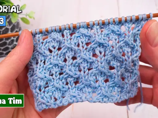 Manos tejiendo un patrón de puntos calados a dos agujas utilisima en hilo azul claro. El tejido muestra un diseño intrincado con agujeros y trenzas.