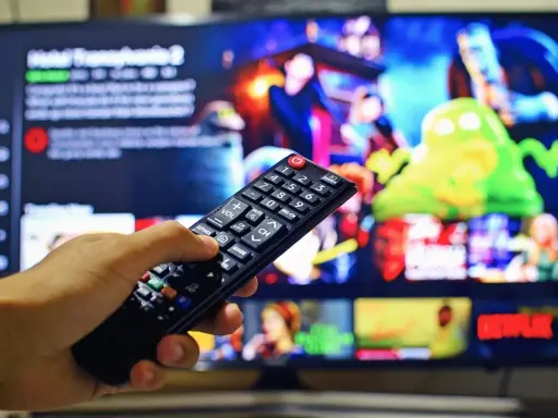 Dłoń trzymająca pilot do telewizora, na ekranie menu platformy streamingowej. Wady i zalety reklamy telewizyjnej – czy warto ją oglądać?