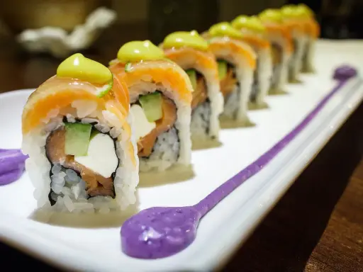 Une délicieuse recette maki original : rouleaux de saumon, avocat, concombre et fromage frais, ornés d'une touche de sauce verte et de purée violette.