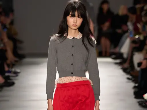 Modella con cardigan grigio e gonna rosso vivo, un contrasto audace.