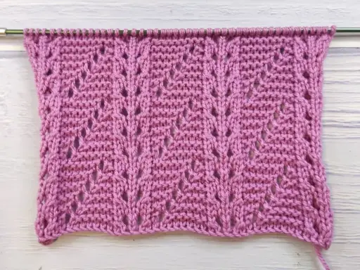 Muestra de tejido con puntos fantasía crochet en color rosa, con un patrón de hojas caladas.