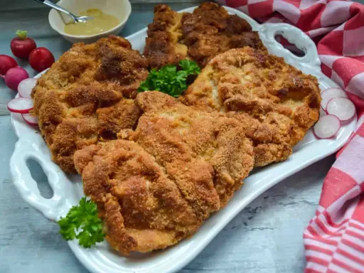 Goldbraun paniertes Schnitzel, perfekt zubereitet, liegt auf einem weißen Teller, garniert mit Petersilie und Radieschen.