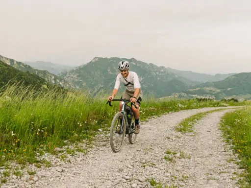 Kolarz na rowerze pokonuje krętą drogę z **gravel co to** w tle górskiego krajobrazu.