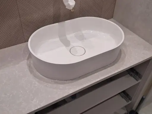 Elegancka łazienka z owalną umywalką nablatową na blacie z konglomeratu kwarcowego. Jasne, subtelne kolory kamienia tworzą spokojną atmosferę.