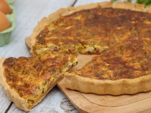 Une part de quiche lorraine dorée, avec sa garniture aux lardons et herbes, prête à être dégustée. La vraie recette quiche lorraine.