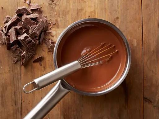 Chocolat fondu qui durcit dans une casserole, avec des morceaux de chocolat à côté sur une planche en bois.
