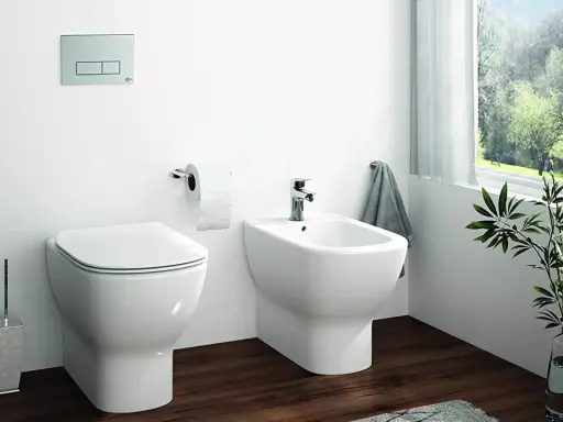 Bagno moderno con wc e bidet affiancati, un discreto muretto dietro nasconde lo scarico. Carta igienica e porta scopino completano l'arredo.