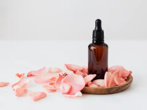 Flacon d'huile essentielle ambré entouré de pétales de rose. Un soin doux pour une femme enceinte.