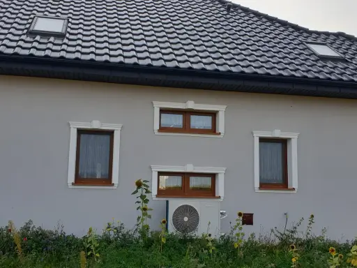 Elegancki gzyms co to? Ozdobne obramowanie okien na szarym domu z brązowymi oknami i słonecznikami.