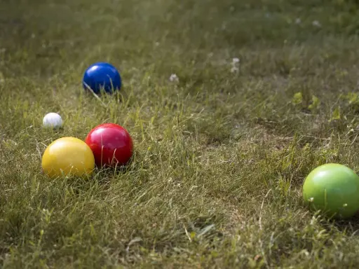 Boules colorées (jaune, rouge, bleu, vert) et une petite blanche sur l'herbe, prêtes pour un concours de pétanque.