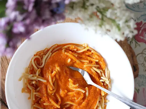 Pyszny przepis na sos do spaghetti, podany z makaronem w białej misce. W tle kwitnące kwiaty.