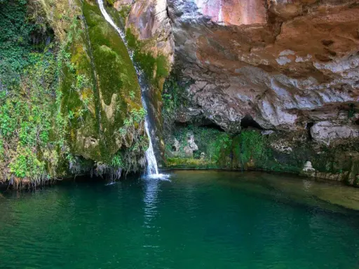 La cascada del río Carbo cae en una poza de agua verde esmeralda, rodeada de rocas cubiertas de musgo y vegetación exuberante.