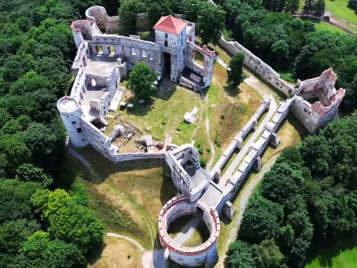 Zamek Rudno, otoczony bujną zielenią, prezentuje się jako malownicza ruina z kamiennymi murami i wieżami.
