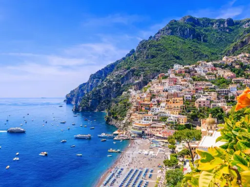 Färgstarka hus klättrar uppför bergssluttningen vid en livlig strand. Perfekt för din resa till Italien tips!