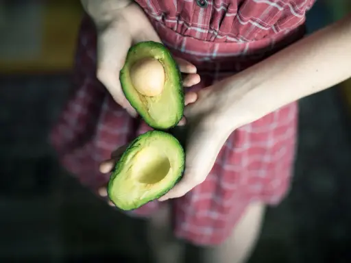 Hände halten eine aufgeschnittene Avocado, bereit für eine pflegende Avocado-Maske für die Haare.