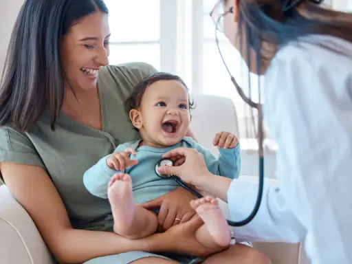 Glad mamma ser sitt barn få ett års vaccin. Läkaren lyssnar på barnets hjärta med stetoskop.