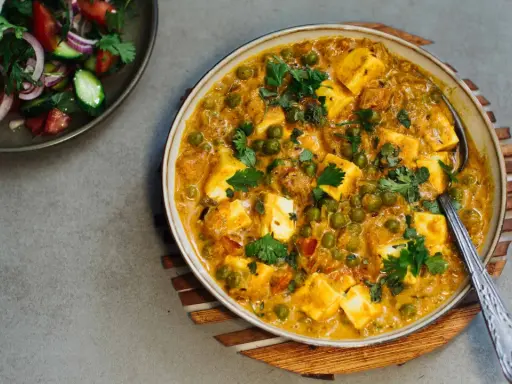 Cremiges Matar Paneer mit Erbsen und würzigen Paneer-Würfeln, garniert mit Koriander. Daneben ein frischer Salat.