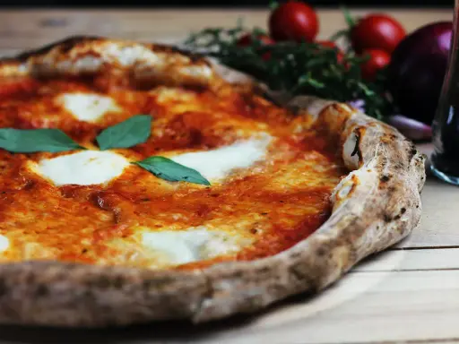 En perfekt pizza på grillen, med smält mozzarella och färsk basilika. Tomater och vitlök i bakgrunden.