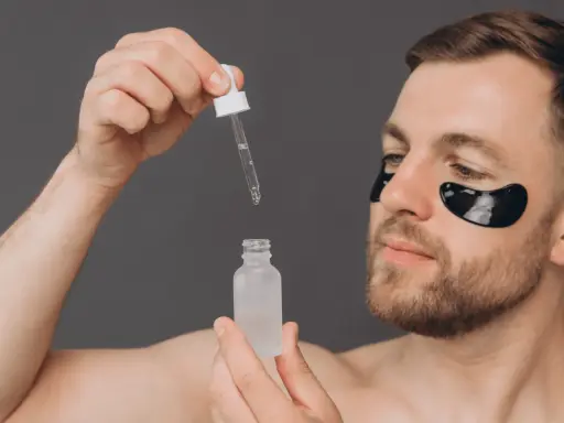 Homme appliquant un sérum, se demandant acide glycolique combien de fois par semaine. Patchs noirs sous les yeux pour un soin ciblé.