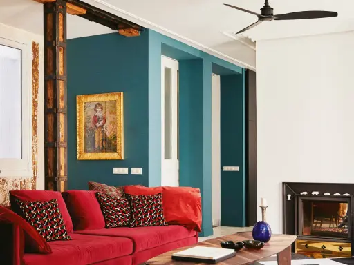 Sofá rojo vibrante con cojines estampados, pared azul petróleo y detalles rústicos. ¡Los mejores colores para pintar una casa!