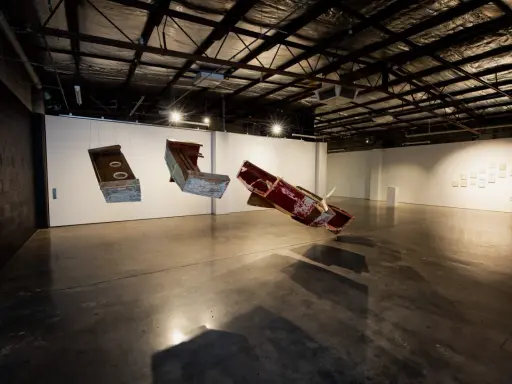 Suspended sculptures of weathered wood and metal hang in the spacious praxis gallery, casting long shadows on the concrete floor.