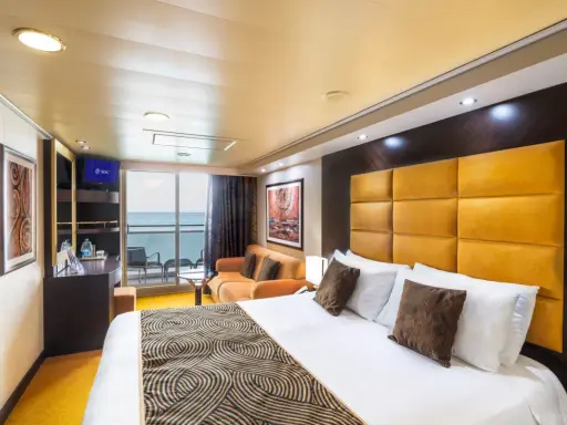Interno di una cabina con balcone MSC Splendida: letto king-size, divano arancione, TV e vista mare.
