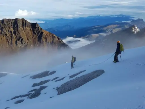 Dwóch alpinistów na ośnieżonym zboczu, w tle majestatyczne góry Ekwadoru, w tym najwyższy szczyt ekwadoru.