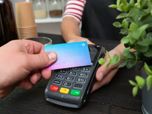 Pago sin contacto con una tarjeta prepago. Una mano acerca una tarjeta de colores a un terminal de pago.