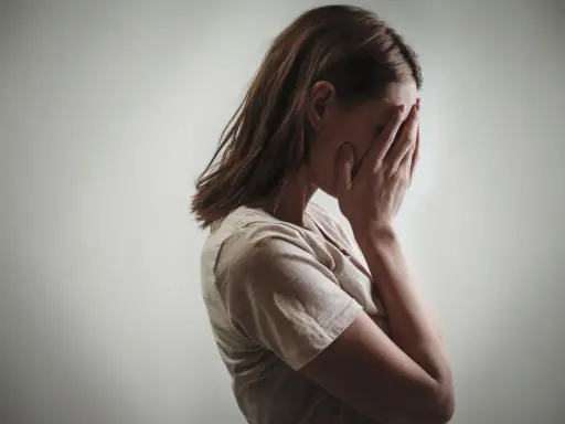 Kobieta zakrywa twarz dłońmi, co może symbolizować różne psychozy objawy, takie jak przytłoczenie czy izolacja.