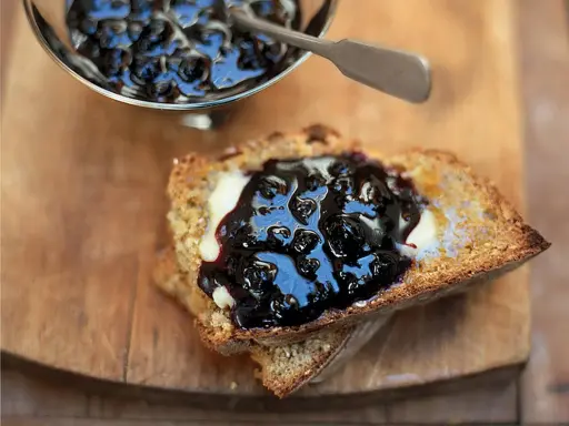 Ein Toast mit Butter und ausgefallener Heidelbeermarmelade, die in einem silbernen Schälchen daneben serviert wird.