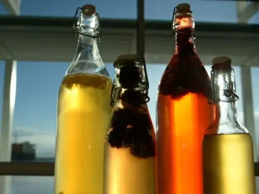 Cztery butelki z napojem, w tym jedna z ciemnymi owocami. To domowa kombucha co to jest? Napój fermentowany, zdrowy i pyszny.