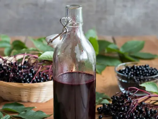 Flasche mit dunklem Saft, daneben Körbchen und Schale mit Holunderbeeren. Achtung: Holunderbeeren giftig!