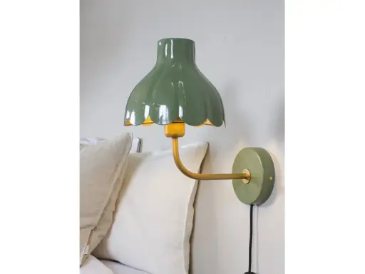 A green scalloped lampshade with a yellow interior, mounted on a gold arm attached to a green wall plate.