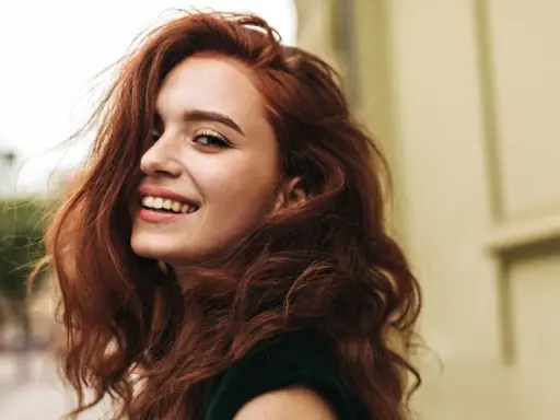 Donna con capelli rossi mossi e un sorriso radioso. La sua chioma è così bella che si può fare la tinta ogni 15 giorni per mantenerla perfetta.
