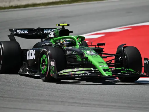 Ein grüner Formel 1 Bolide mit KICK-Sponsorenaufdruck rast auf der Rennstrecke. Die leistungsstarken Formel 1 Motoren lassen ihn über den Asphalt fliegen.