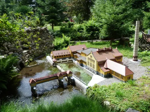 Miniaturowa zabudowa z mostkiem i rzeką, jak w parkach miniatur w Polsce.