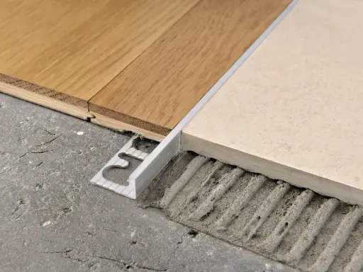 Un battiscopa metallico crea abbinamenti quando mancano le piastrelle del pavimento, unendo legno e ceramica su un sottofondo grezzo.