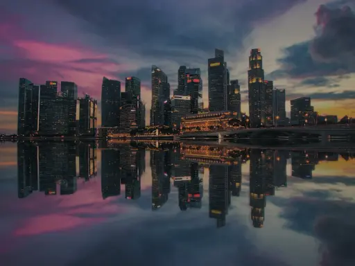 Wieżowce w Singapurze odbijają się w wodzie o zachodzie słońca. To miasto-państwo, gdzie leży Singapur, zachwyca nowoczesną architekturą.