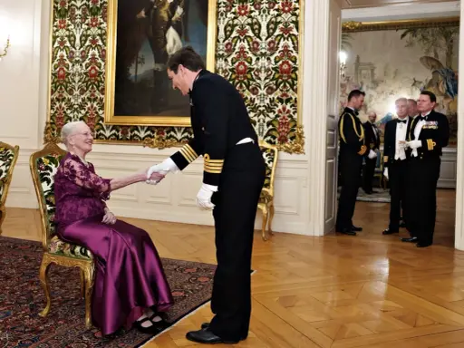 Drottning Margrethe, trots att hon är sjuk, tar emot en officer med ett leende. Hon sitter i en elegant stol, klädd i en lila klänning.