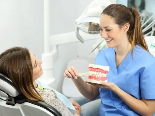 Uśmiechnięta higienistka stomatologiczna pokazuje pacjentce, jak prawidłowo szczotkować zęby na modelu szczęki.