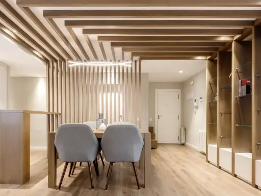 Comedor moderno con separador de listones de madera y estanterías. Preguntarse cuanto se tarda en tirar un tabique es irrelevante aquí.