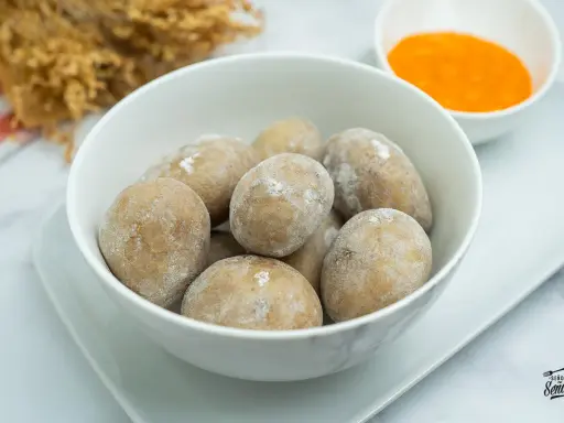 Un tazón blanco lleno de papas arrugadas, cubiertas de sal, junto a un pequeño cuenco con mojo rojo.