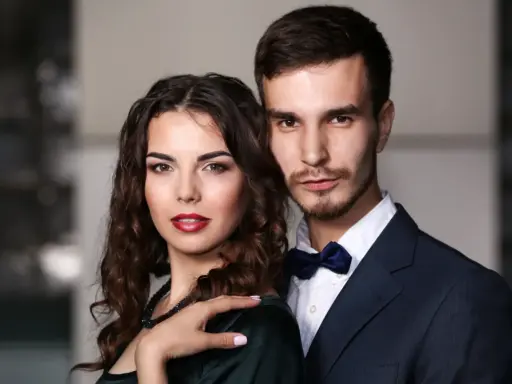 Elegancka para, niczym koziorożec i baran, pozuje do zdjęcia. Ona w ciemnej sukni, on w granatowym garniturze.