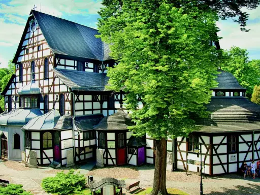 Kościół Pokoju w Świdnicy, z charakterystyczną szachulcową architekturą, otoczony zielenią.