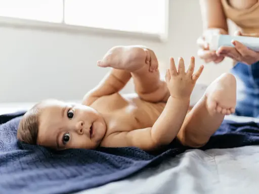 Uroczy noworodek leży na granatowym kocyku, podnosząc nóżki. Mama przygotowuje się do masażu brzuszka, by ulżyć mu w **gazach u noworodka**.