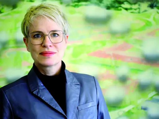 Frauke Burgdorff, eine Frau mit kurzen blonden Haaren und Brille, blickt lächelnd in die Kamera. Sie trägt einen grauen Blazer.