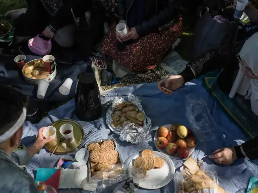 Familie feiert Fastenbrechen im Islam mit Picknick im Freien. Kekse, Früchte und Kaffee werden geteilt.
